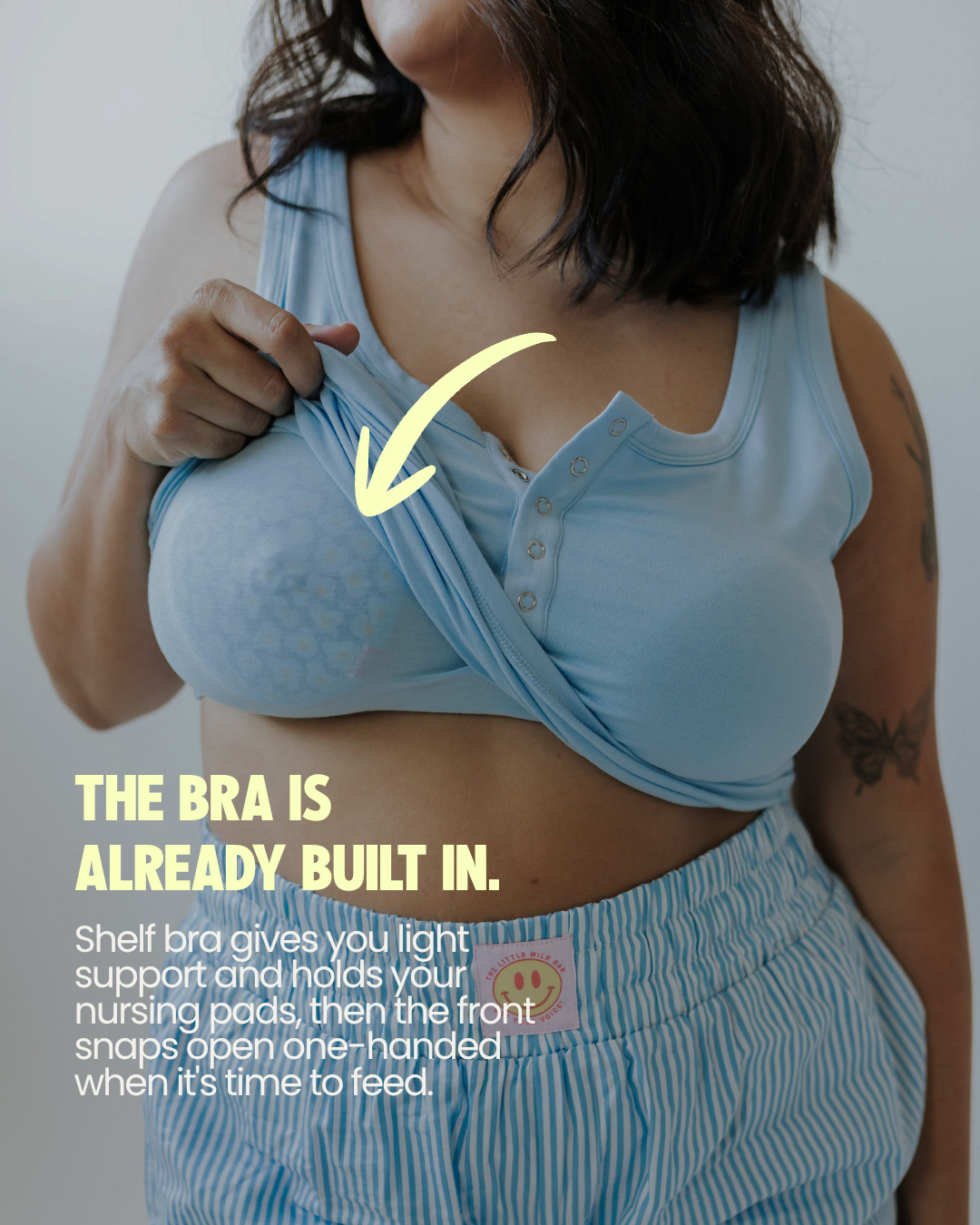 Mom lifting the Postpartum Tank to show the built-in shelf bra holding a nursing pad, with front snaps for easy nursing access